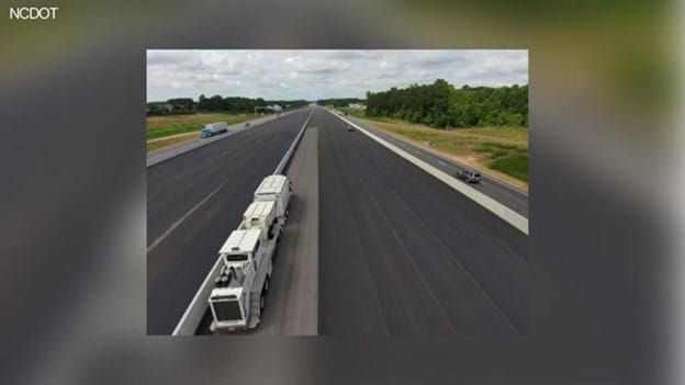 Aerial view of a wide, empty highway with vehicles traveling in both directions, including a large truck and several cars.