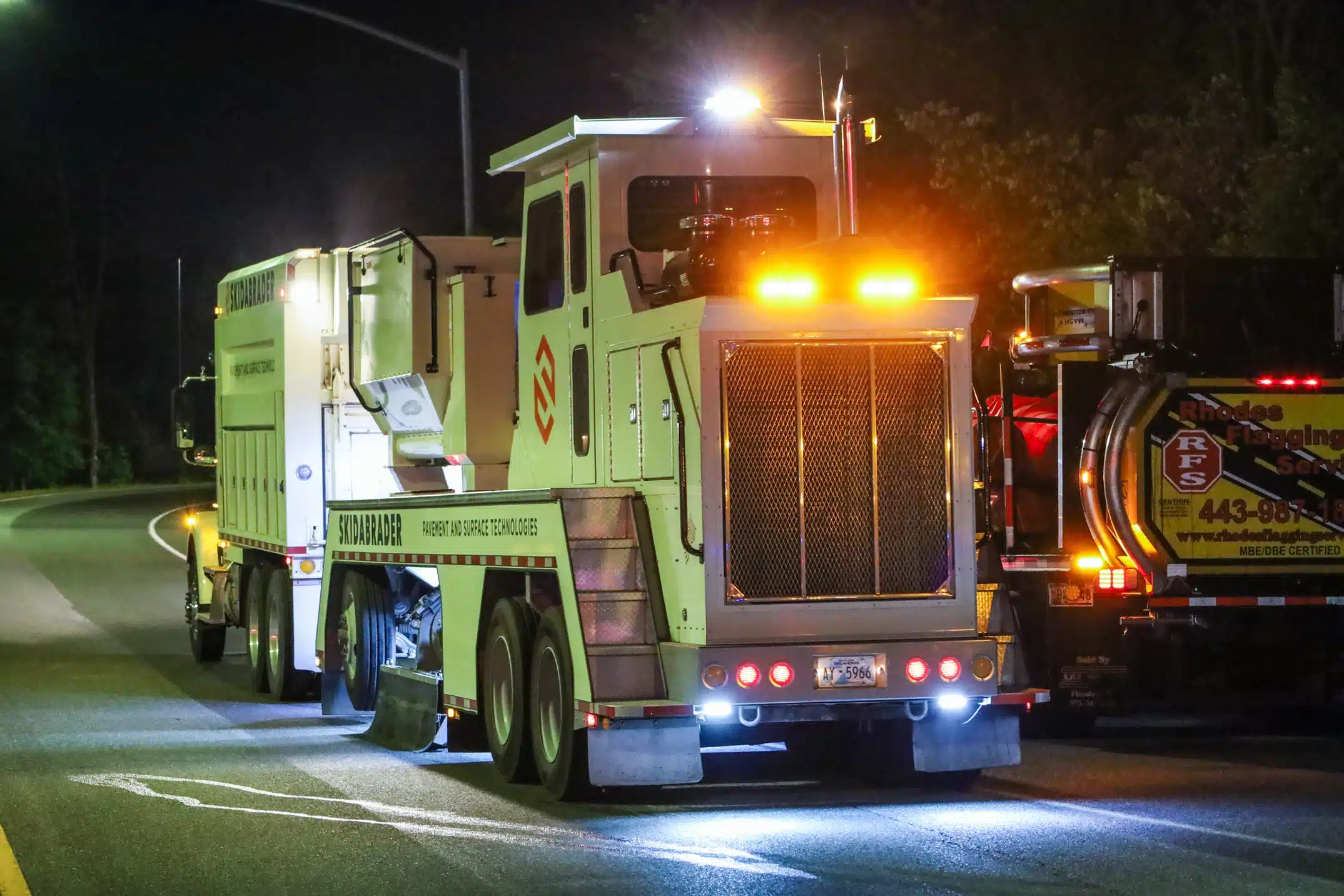 A large paver truck with flashing lights on a dark road at night.