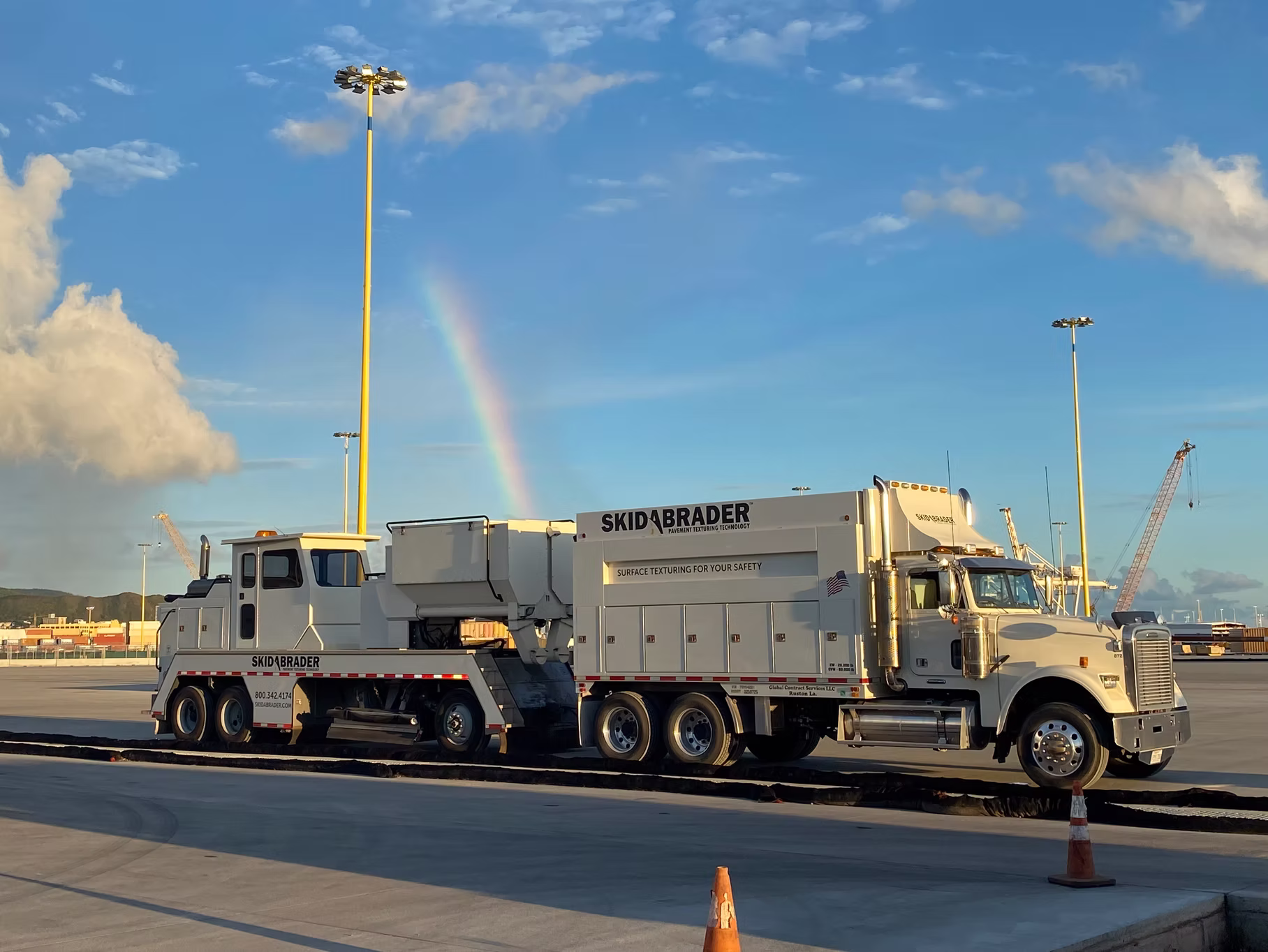 Skidabrader truck on highway with rainbow in a clear blue sky