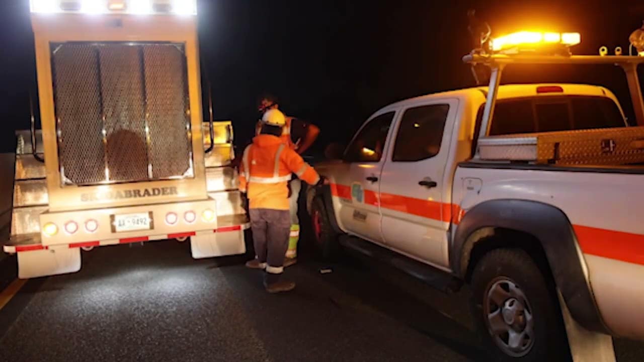 large truck and pickup truck with lights at night. two construction workers in orange and yellow hats